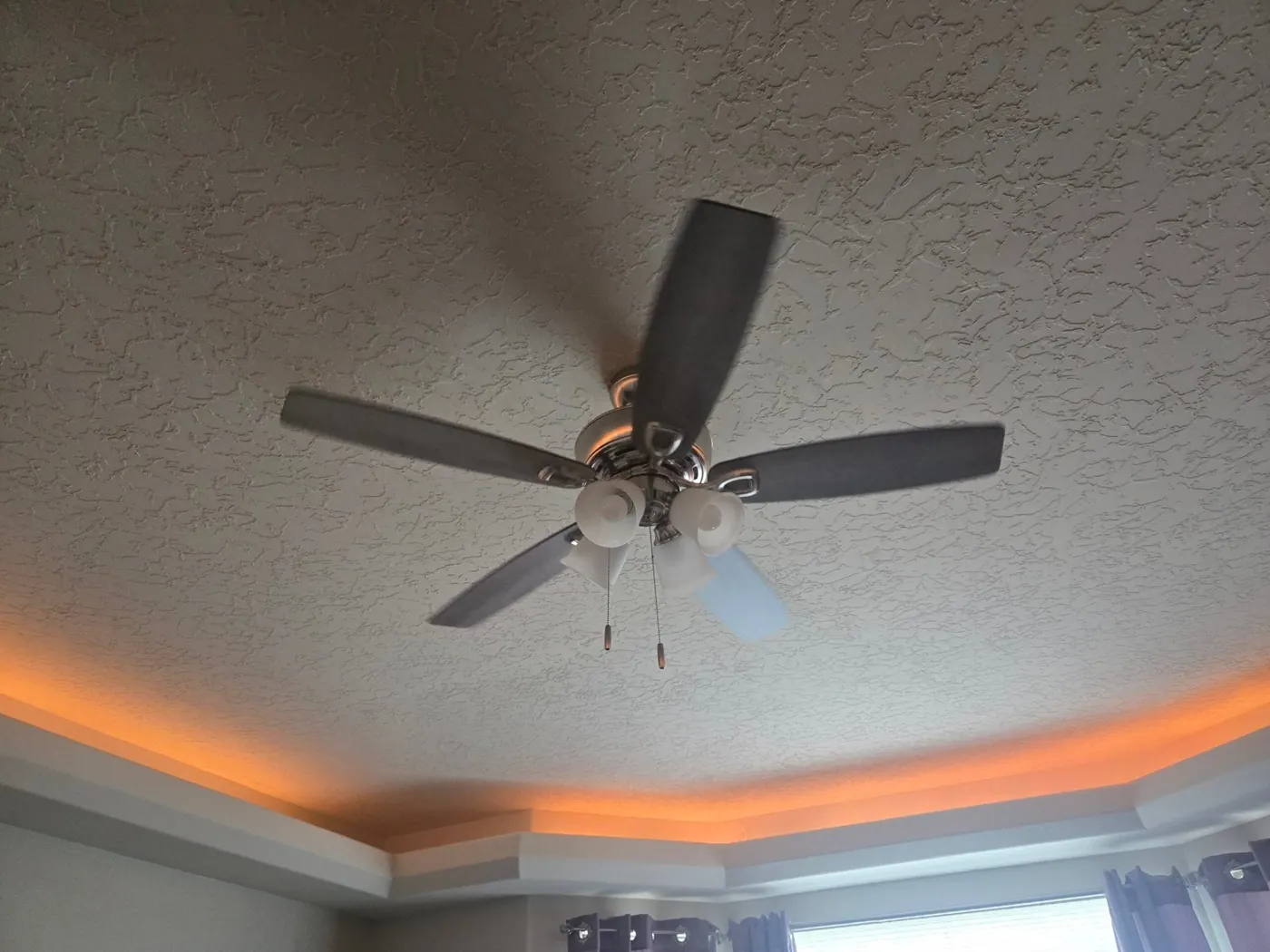 A ceiling fan with lights in a tray ceiling lit by warm LED cove lighting