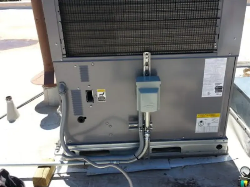 A rooftop HVAC unit with a newly mounted gray power disconnect box and conduit