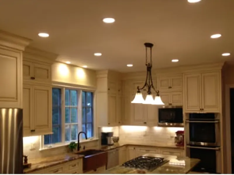 A kitchen with three pendant lights over the island, recessed ceiling lights and lit under-cabinet strips