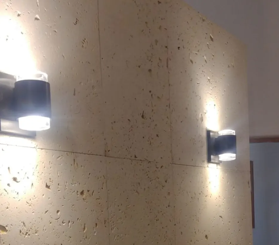 Two black up-and-down wall sconces casting light on a travertine stone wall