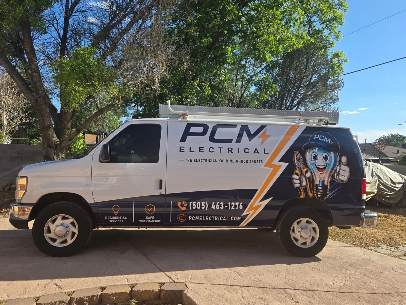 The PCM Electrical van, wrapped in navy and white with an orange lightning bolt, the bulb mascot and the phone number (505) 463-1276